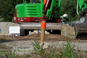 Met stevige piketpalen wordt aangegeven waar het tracé van de nutsleidingen op de bouwplaats ligt. Zwaar materieel mag er niet overheen rijden. 